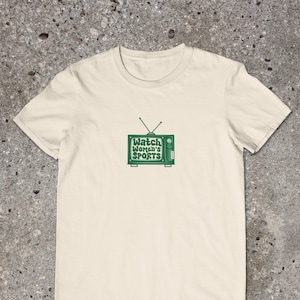 May include: A cream colored t-shirt with a green retro television graphic that says "Watch Women's Sports" on the screen.