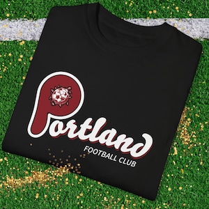 May include: Black t-shirt with a red and white "Portland Football Club" logo. The logo features a stylized "P" with a soccer ball inside.