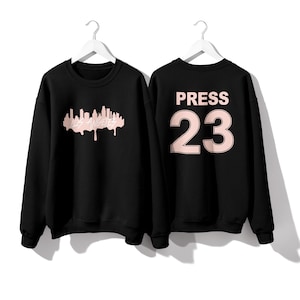 May include: Two black sweatshirts with pink text. One sweatshirt has a graphic of the Los Angeles skyline with the text "Los Angeles" dripping below. The other sweatshirt has the text "PRESS 23" on the back.