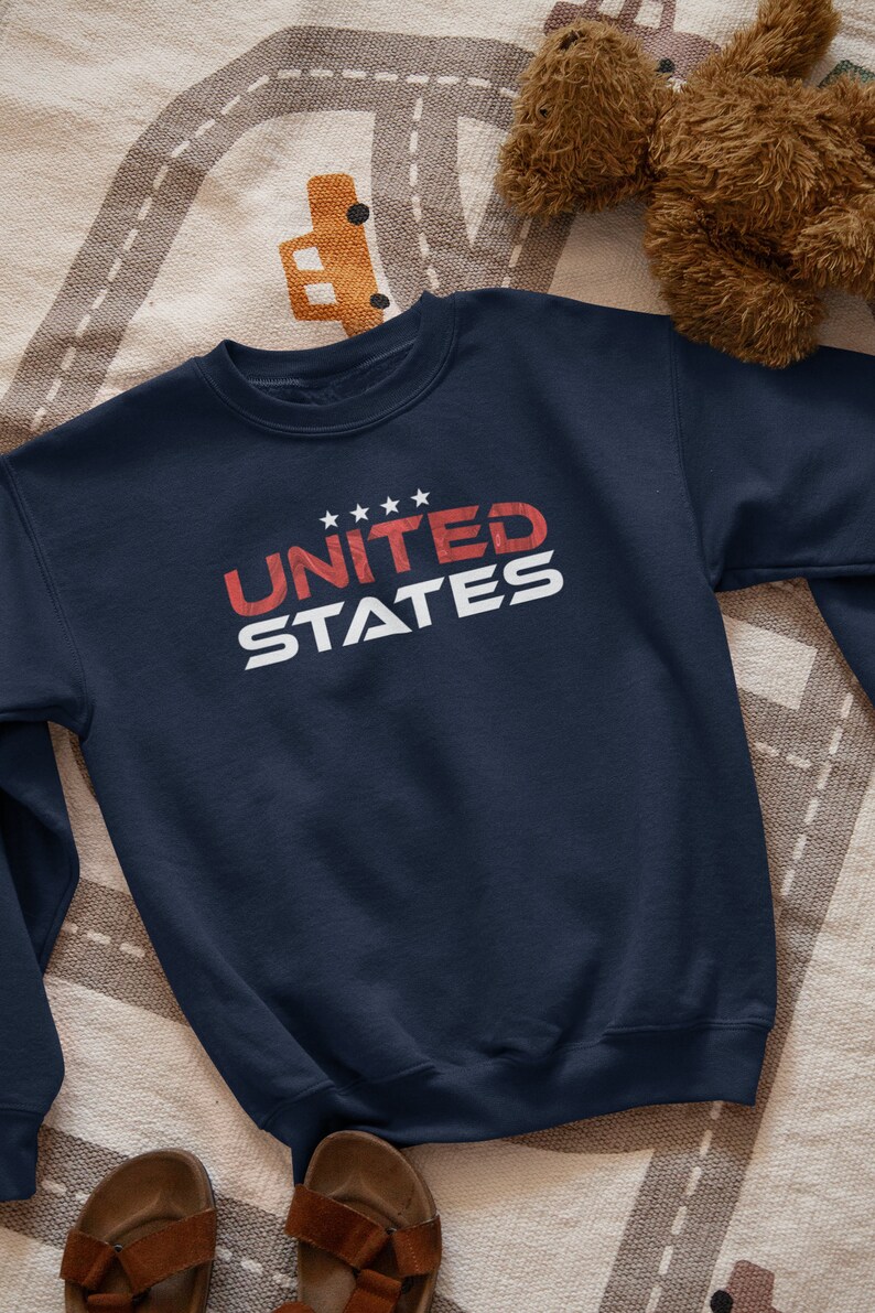Op de afbeelding: Een donkerblauw sweatshirt met de tekst "UNITED STATES" in rood en wit. De tekst is gestyled met een vintage look.