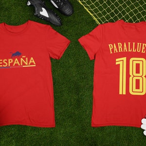 May include: Red soccer jersey with the word "ESPA&Ntilde;A" and a bull graphic on the front and the name "PARALLUELO" and the number "18" on the back.