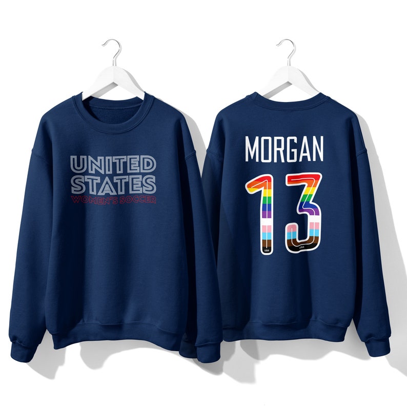 Puede incluir: Una sudadera azul marino con el texto "UNITED STATES WOMEN'S SOCCER" en la parte delantera y el texto "MORGAN 13" en la parte posterior. El n&uacute;mero 13 est&aacute; contorneado en colores arco&iacute;ris.
