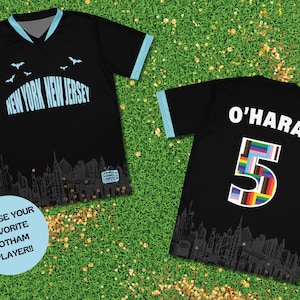 K&ouml;nnte beinhalten: Schwarzes Fu&szlig;balltrikot mit einem Skyline-Motiv und dem Text "NEW YORK NEW JERSEY" auf der Vorderseite. Die R&uuml;ckseite des Trikots tr&auml;gt den Namen "O'HARA" und die Nummer "5" mit einem Regenbogenflaggen-Design.