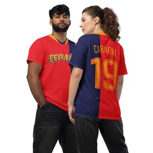 May include: Two people wearing soccer jerseys. The jersey on the left is red and has the word "ESPAI" on it. The jersey on the right is blue and red and has the name "CARMONA" and the number "19" on it.