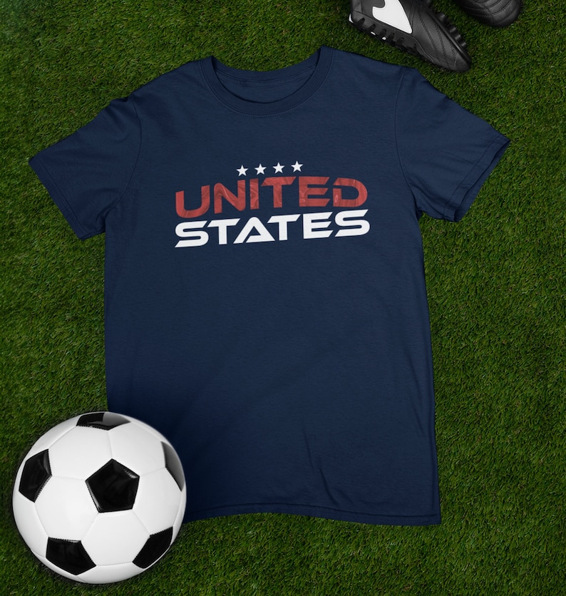 Op de afbeelding: Een marineblauw t-shirt met een witte afbeelding waarop "UNITED STATES" in rode letters staat met vijf witte sterren boven het woord "UNITED".