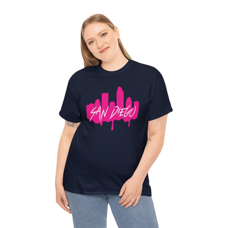 May include: A navy blue t-shirt featuring a pink graphic of the San Diego skyline. The skyline is dripping with pink paint.