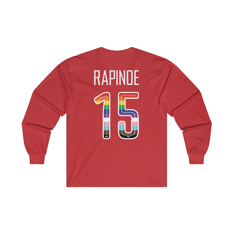 Op de afbeelding: Rood langarm T-shirt met de naam "RAPINOE" en het nummer "15" in regenboogkleuren op de achterkant.