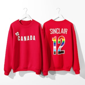 May include: Red sweatshirt with a white maple leaf and the word "CANADA" on the front and the name "SINCLAIR" and the number "12" with a rainbow design on the back.