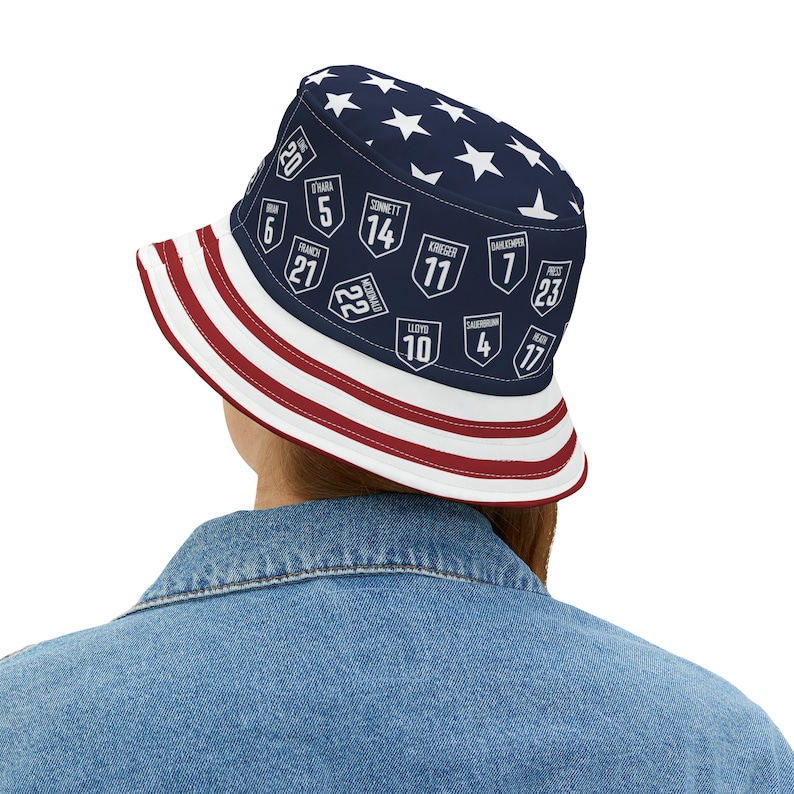 May include: A blue and white bucket hat with red stripes and white stars. The hat has a pattern of white numbers and names on a blue background.