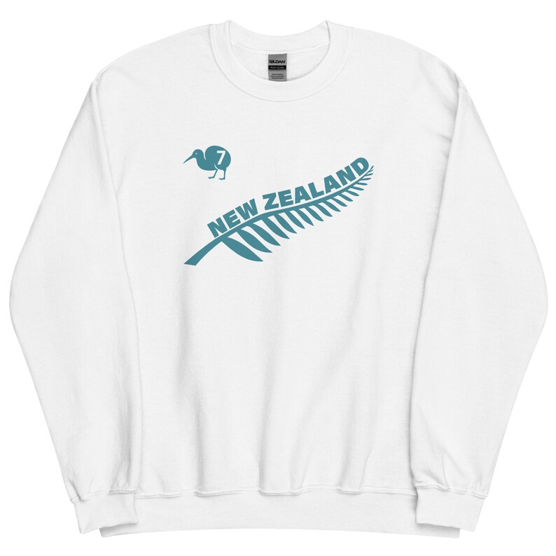 May include: White sweatshirt featuring a teal green fern leaf design with the words "NEW ZEALAND" printed on the leaf. A teal green kiwi bird with the number "7" is positioned above the leaf.