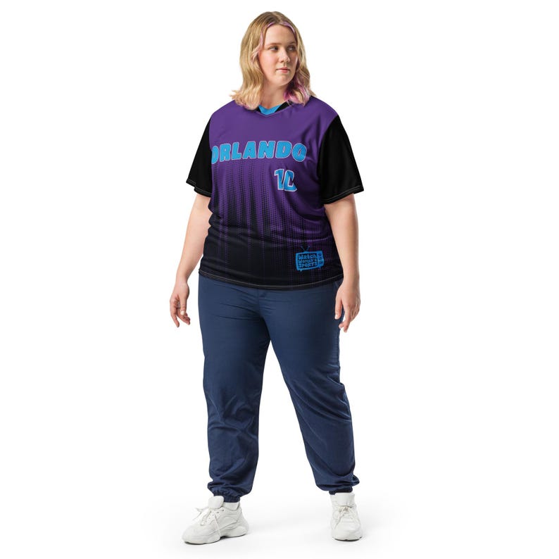 Op de afbeelding: Een paars en zwart shirt met het woord "ORLANDO" en het nummer "12" in blauw. Het shirt heeft een zwart-wit patroon aan de onderkant.