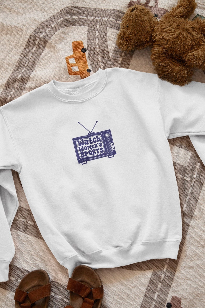 May include: White sweatshirt with a blue vintage television graphic that says "Watch Women's Sports".