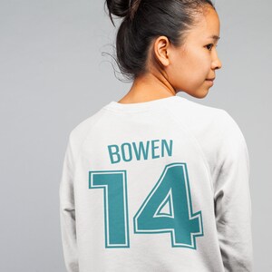 May include: White sweatshirt with a teal blue number "14" and the name "BOWEN" printed on the back.