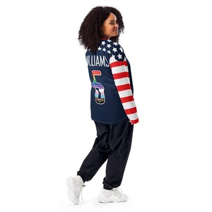 May include: A navy blue long-sleeved jersey with a white and red American flag design on the sleeves. The jersey has the number "5" on the back with a rainbow design and the word "WILLIAMS" above it.