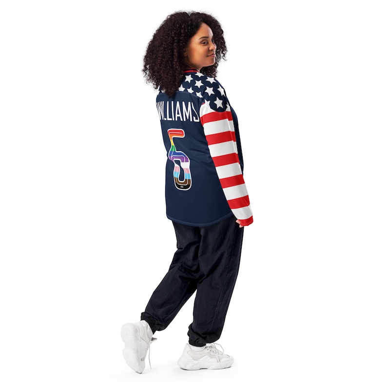 May include: A navy blue long-sleeved jersey with a white and red American flag design on the sleeves. The jersey has the number "5" on the back with a rainbow design and the word "WILLIAMS" above it.