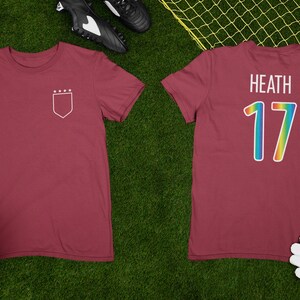 May include: A maroon soccer jersey with a white shield and stars on the front and the name "Heath" and the number "17" in rainbow colors on the back.