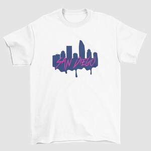 May include: White t-shirt featuring a navy blue silhouette of the San Diego skyline with the text "SAN DIEGO" in pink dripping paint.
