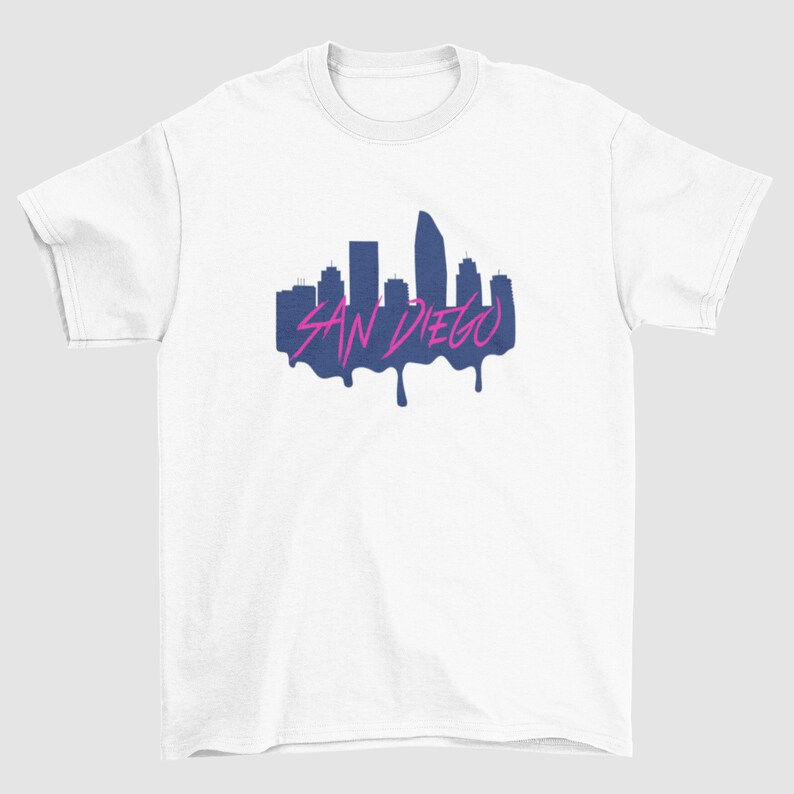 May include: White t-shirt featuring a navy blue silhouette of the San Diego skyline with the text "SAN DIEGO" in pink dripping paint.
