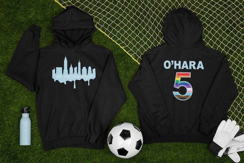 Puede incluir: Dos sudaderas con capucha negras. Una tiene una silueta azul del horizonte de la ciudad de Nueva York con el texto "Nueva York, Nueva Jersey" debajo. La otra sudadera con capucha tiene el texto "O'HARA" y el n&uacute;mero "5" en colores arco&iacute;ris en la parte posterior.
