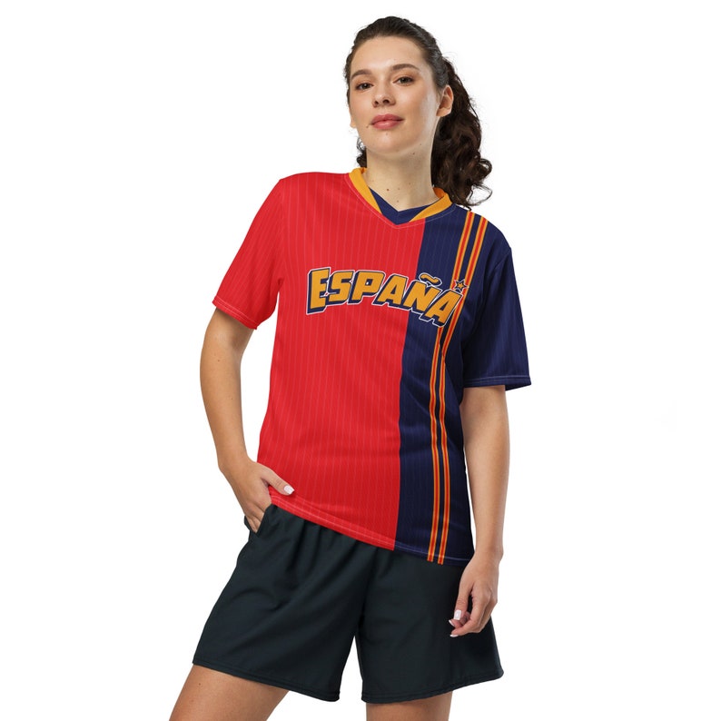 May include: A red and navy blue soccer jersey with the word "ESPA&Ntilde;A" in yellow lettering. The jersey has a striped pattern and a v-neck.