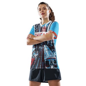 Op de afbeelding: Een blauw en wit shirt met een grafische print van een trein en het woord "CHICAGO" op de voorkant. Het shirt wordt gedragen door een persoon met gekruiste armen.