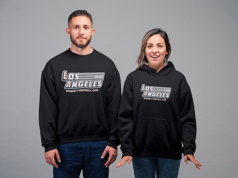 Pu&ograve; includere: Felpa e felpa con cappuccio nere con la scritta "Los Angeles Women's Football Club" in un design stilizzato. Il testo &egrave; in bianco, grigio e rosa. La felpa ha lo scollo tondo e la felpa con cappuccio ha il cappuccio con coulisse.