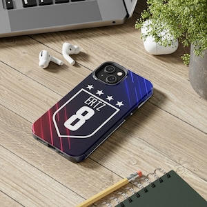 May include: A blue and red phone case with a white shield design. The shield has the text "ERTZ" and the number "8" inside. There are five white stars above the text.