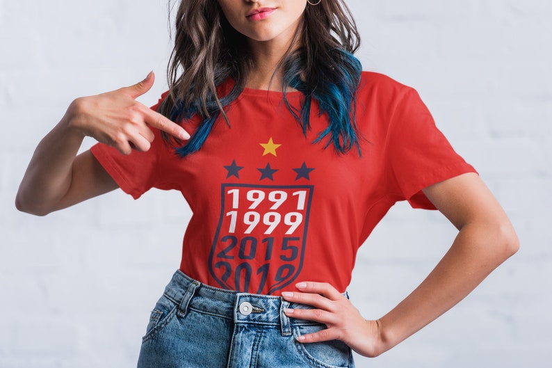 Puede incluir: Camiseta roja con un gr&aacute;fico blanco de un escudo con cuatro estrellas y los a&ntilde;os 1991, 1999, 2015 y 2019.