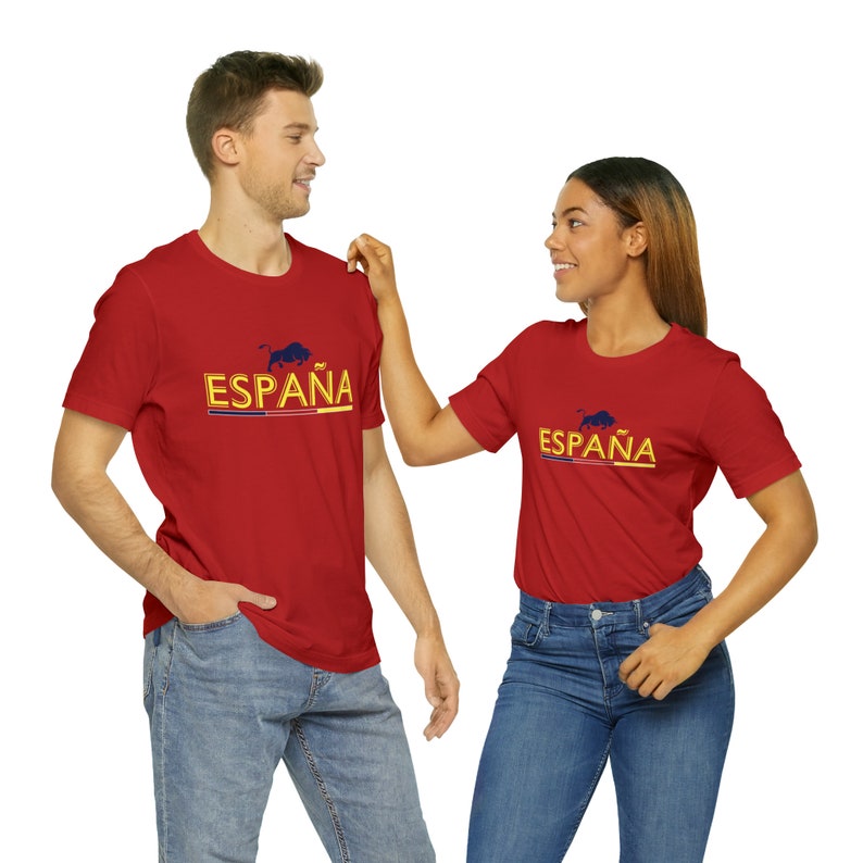 May include: Two people wearing red t-shirts with the word "ESPA&Ntilde;A" and a bull graphic printed on the front. The shirts are a bright red color and the text is in a yellow and blue font.