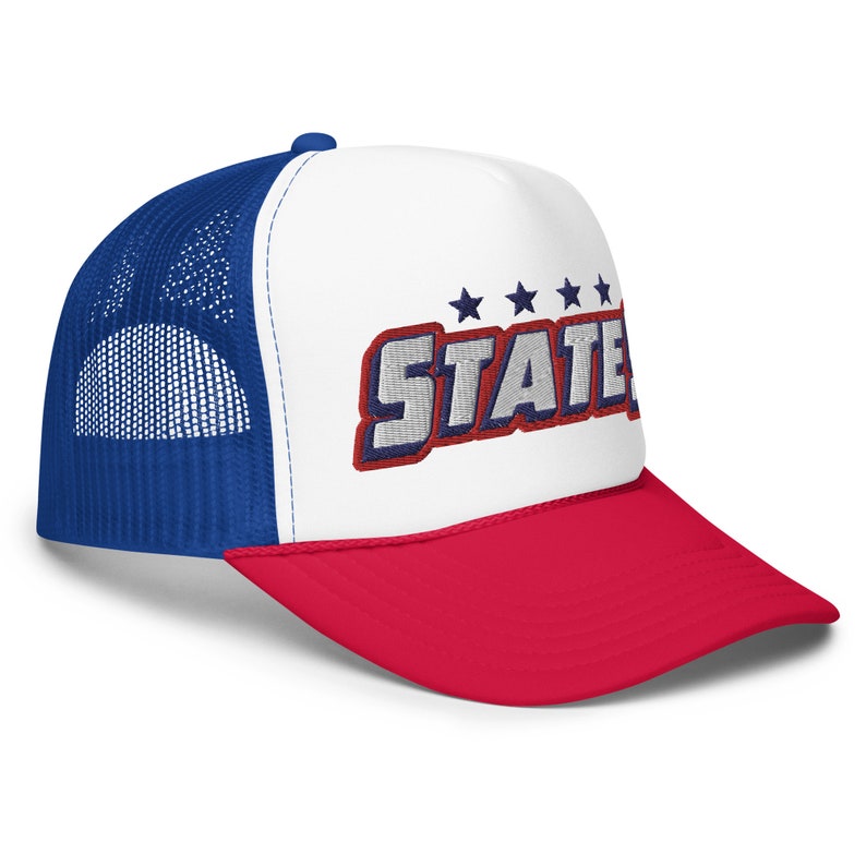 Puede incluir: Una gorra de camionero blanca, azul y roja con una parte trasera de malla. La parte delantera de la gorra tiene un fondo blanco con la palabra "STATE" en letras azules y rojas con cinco estrellas sobre la palabra. La visera de la gorra es roja.