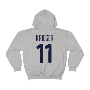 Może przedstawiać: Szara bluza z kapturem z nadrukiem imienia "Krieger" i numeru "11" na plecach w kolorze granatowym.