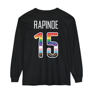 Op de afbeelding: Zwart longsleeve shirt met de naam "RAPINOE" en het nummer "15" in regenboogkleuren op de achterkant.