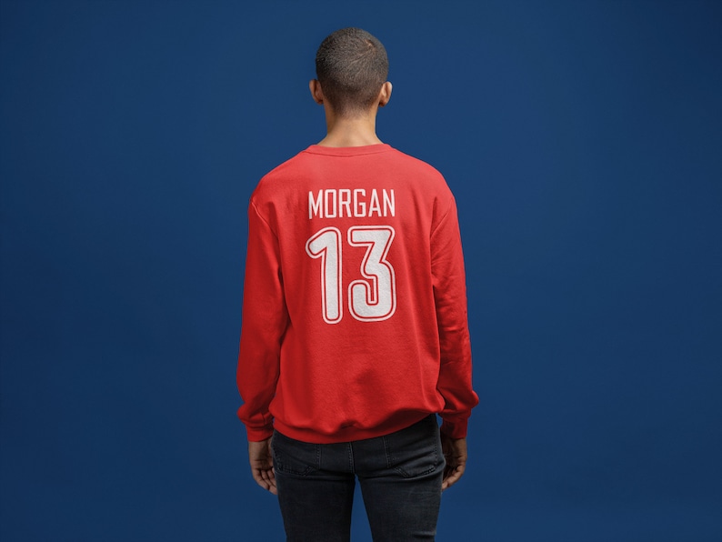 K&ouml;nnte beinhalten: Roter Pullover mit wei&szlig;em Text auf der R&uuml;ckseite, der "MORGAN 13" lautet.