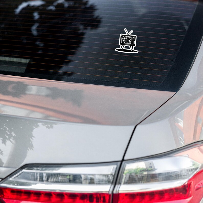 May include: A white car with a sticker on the back window. The sticker is a black and white illustration of a television with the text "Watch Woman's Sports" inside.