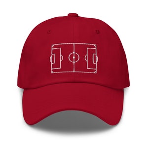May include: A red baseball cap with a white embroidered outline of a football pitch.