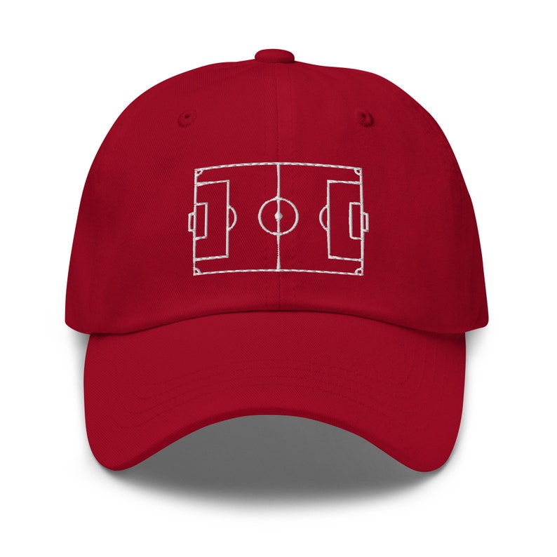 May include: A red baseball cap with a white embroidered outline of a football pitch.