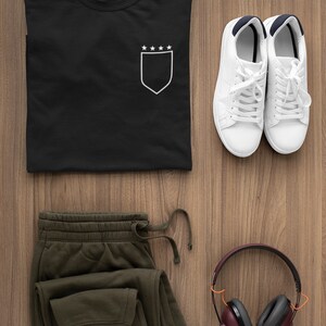 May include: A black t-shirt with a white pocket and five stars on the pocket. A pair of white sneakers, green sweatpants, and brown headphones are also pictured.