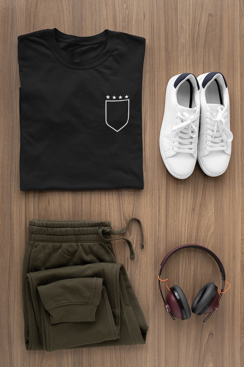 May include: A black t-shirt with a white pocket and five stars on the pocket. A pair of white sneakers, green sweatpants, and brown headphones are also pictured.