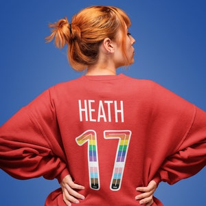 May include: Red sweatshirt with the name "Heath" and the number "17" printed on the back. The number is outlined in rainbow colors.