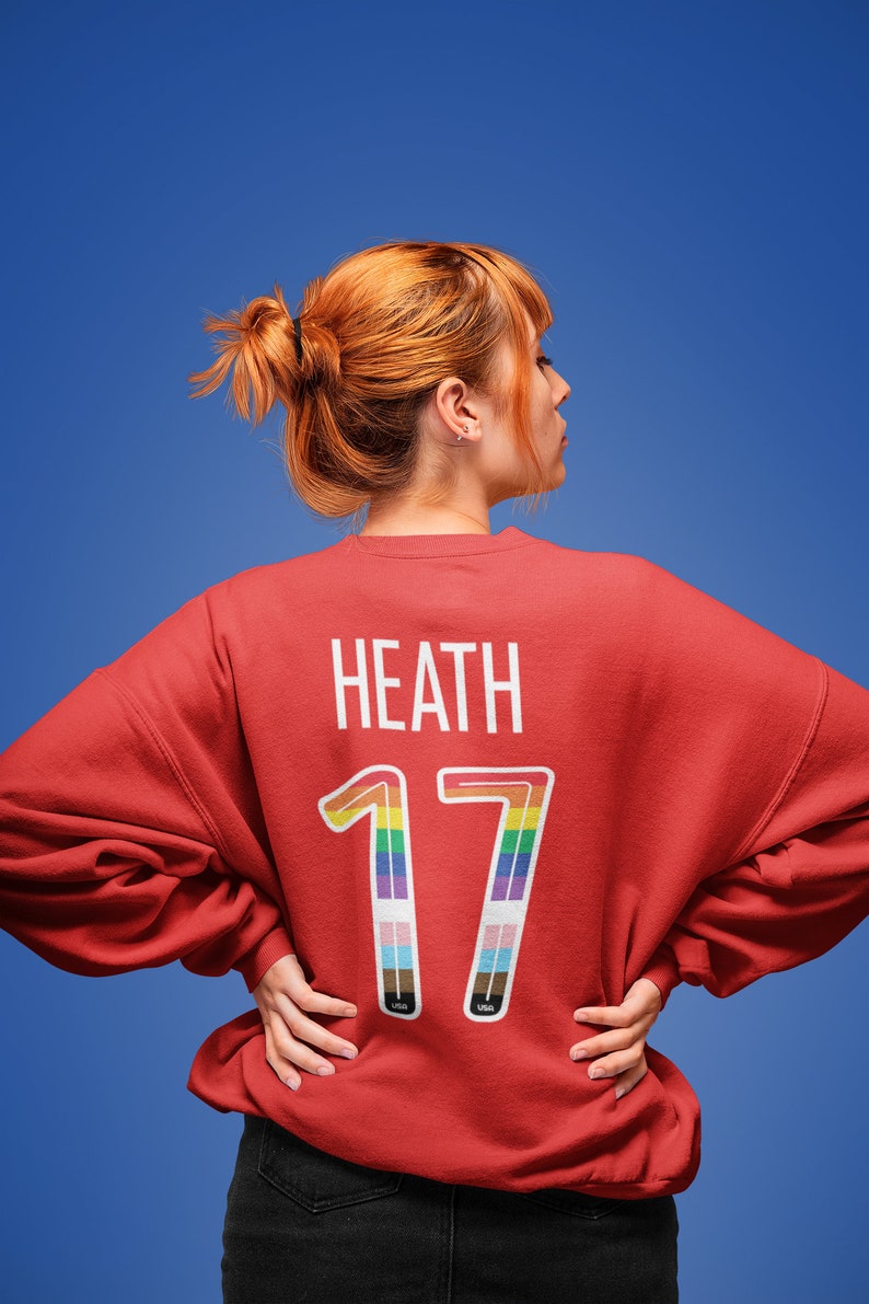 May include: Red sweatshirt with the name "Heath" and the number "17" printed on the back. The number is outlined in rainbow colors.