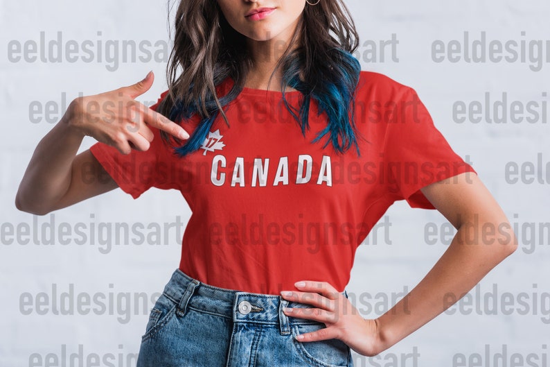 May include: A red t-shirt displaying the word "CANADA" in white capital letters. Above the word is a white maple leaf with the number "17". The person in the image is wearing blue denim jeans.