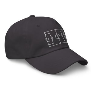 May include: A dark grey baseball cap with a white outline of a football pitch embroidered on the front.