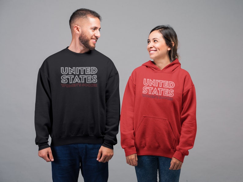 Puede incluir: Dos personas vistiendo sudaderas con el texto "UNITED STATES WOMEN'S SOCCER" impreso en ellas. La persona de la izquierda lleva una sudadera negra y la persona de la derecha lleva una sudadera roja.