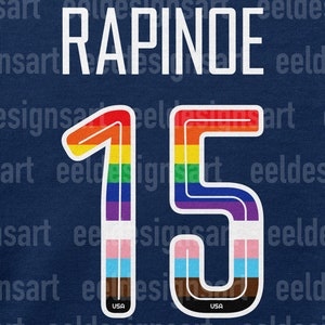 K&ouml;nnte beinhalten: Ein blaues Trikot mit dem Namen "RAPINOE" und der Nummer "15" in Regenbogenfarben. Die Nummer ist wei&szlig; umrandet und hat unten eine kleine US-Flagge.