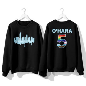 May include: Two black sweatshirts. One sweatshirt has a blue outline of the New York City skyline with the text "New York/New Jersey". The other sweatshirt has the text "O'HARA" and the number "5" with a rainbow design.