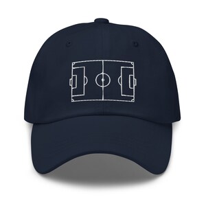 May include: A navy blue baseball cap with a white embroidered outline of a football pitch.