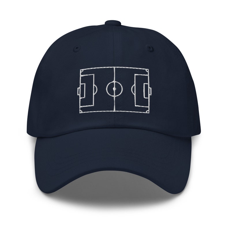 May include: A navy blue baseball cap with a white embroidered outline of a football pitch.
