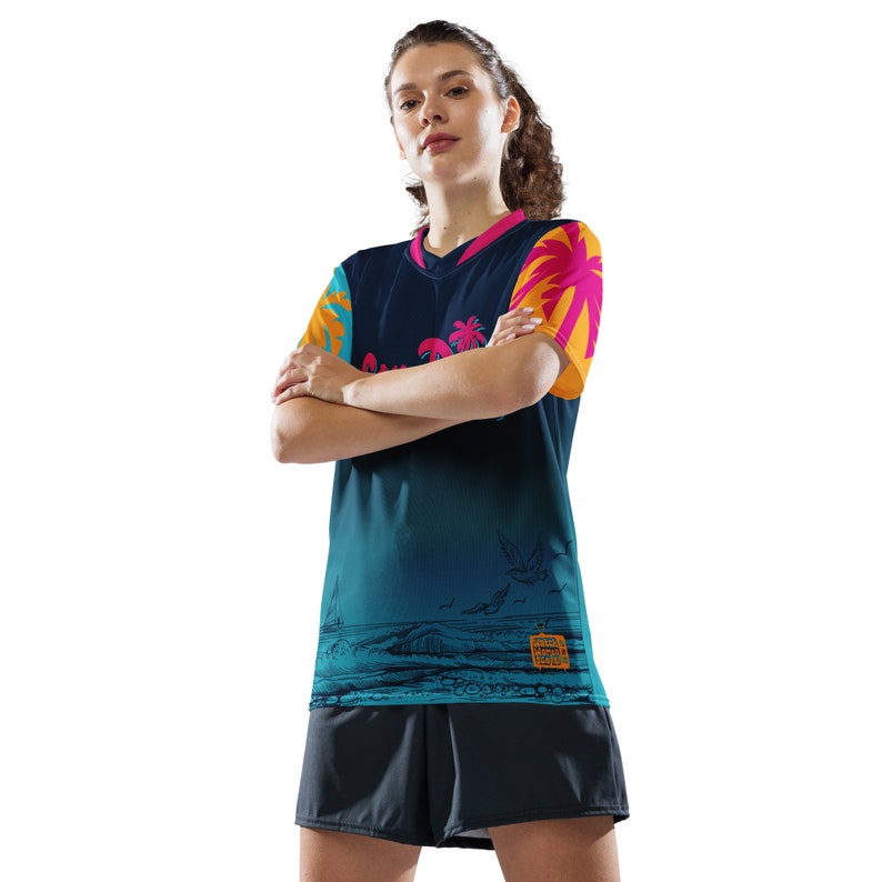 May include: A woman wearing a blue, teal, pink, and orange short-sleeved jersey with a tropical print and a black pair of shorts. The jersey has a graphic of a beach scene with palm trees, birds, and waves. The jersey also has the text "Summer Vibes" on it.