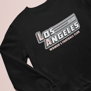 Pu&ograve; includere: Felpa nera con la scritta "LOS ANGELES WOMEN'S FOOTBALL CLUB" in bianco, grigio e rosa. Il testo "EST. 2020" &egrave; sopra la parola "LOS ANGELES". La felpa ha un girocollo e maniche lunghe.