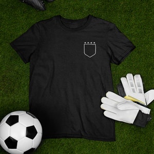 May include: Black t-shirt with a white outline of a shield and five stars on the left chest.